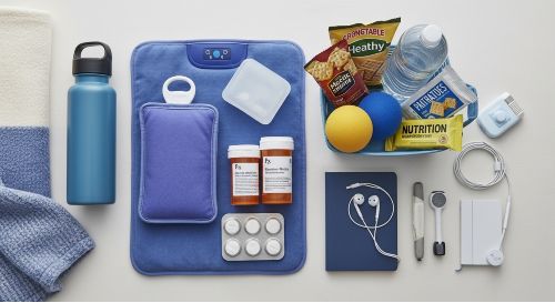 Organized flare-up kit with heating pad, medications, comfort items, and healthy snacks on white background